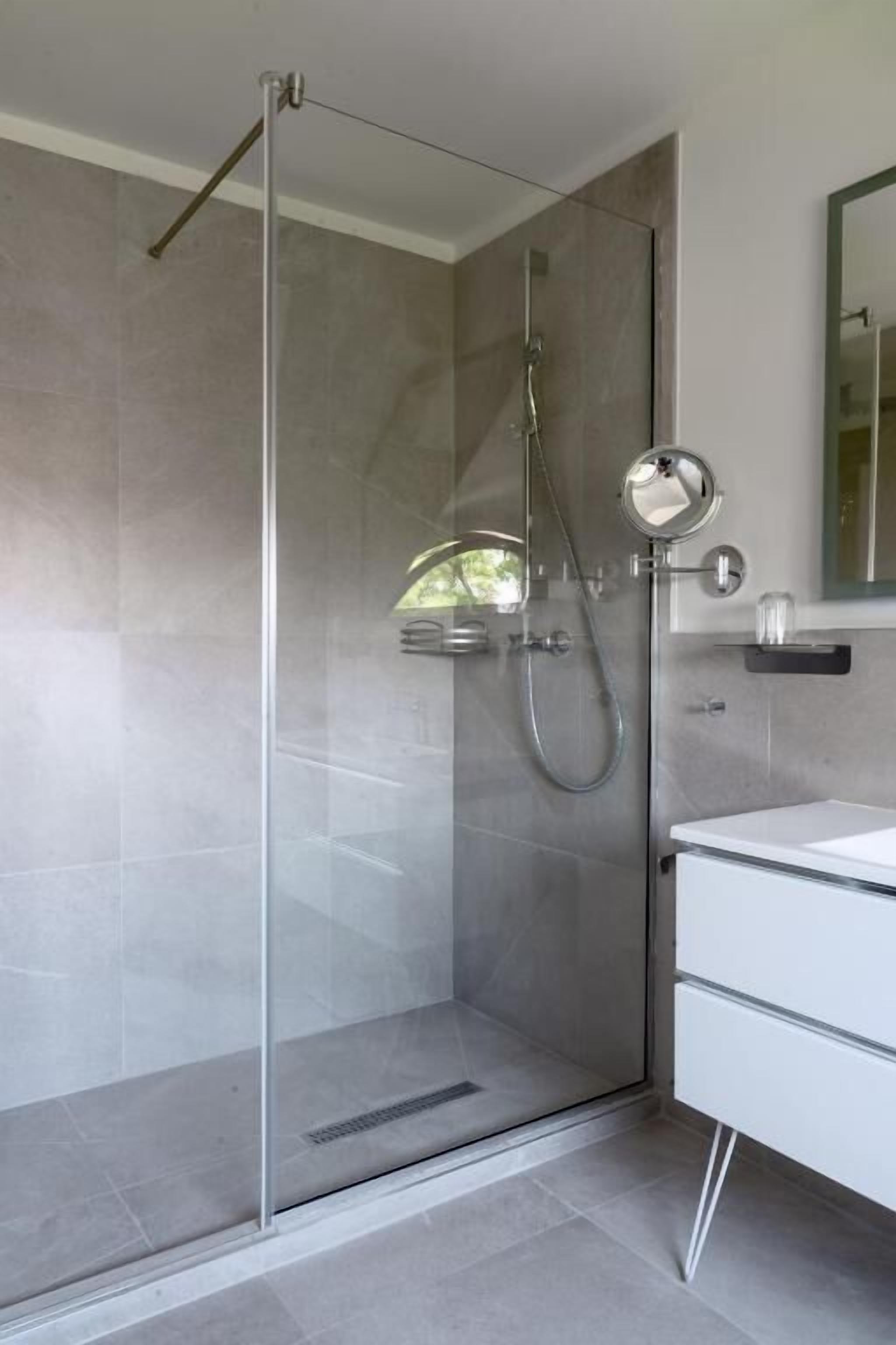 A modern bathroom with a glass-enclosed shower, a white vanity, and a mirror.