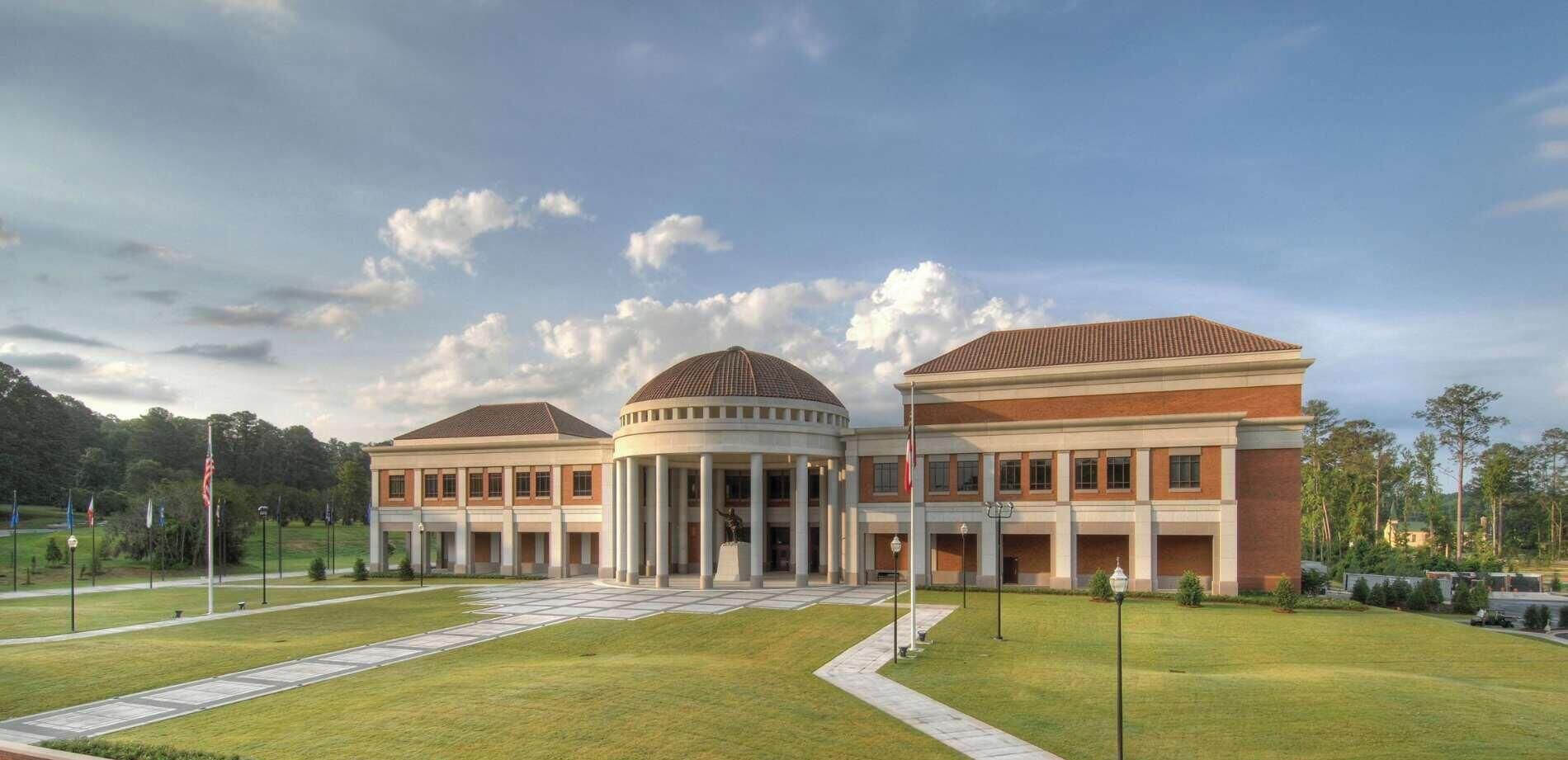 A large building with a central dome and two wings, surrounded by a well-maintained lawn and flagpoles.