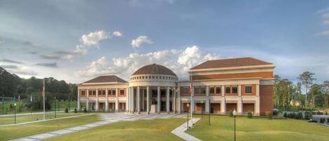 A large building with a central dome and two wings, surrounded by a well-maintained lawn and flagpoles.