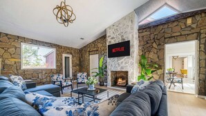 A living room with a stone wall, a fireplace, a Netflix sign, and a large sofa. - Historic Brick Retreat w/ Pool & Games (Columbus)