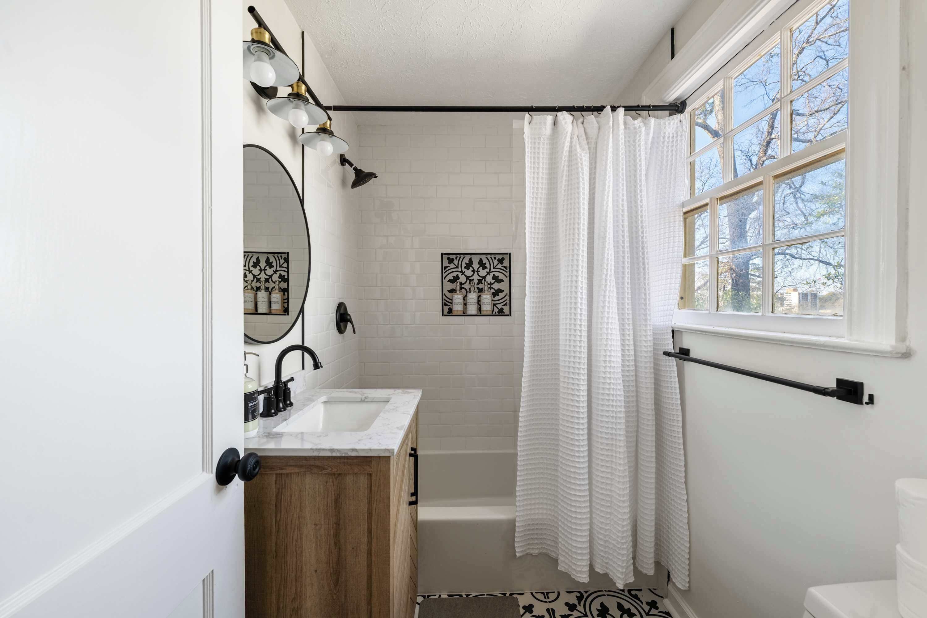 A bathroom with a double sink, a bathtub, a shower curtain, a window, and a wall-mounted towel rack.