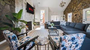 A living room with a stone wall, a fireplace, a sectional sofa, and a TV displaying 'NETFLIX'. - Historic Brick Retreat w/ Pool & Games (Columbus)