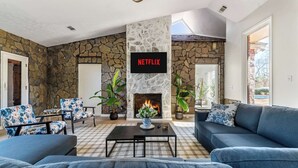 A living room with a stone wall, a fireplace, a Netflix sign, and blue furniture. - Historic Brick Retreat w/ Pool & Games (Columbus)