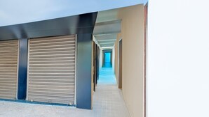 A corridor with closed shuttered doors, a tiled floor, and a straight path leading to a bright interior. - Single Room Swagatam International Airport (Barakpur)