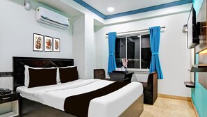 A modern hotel room with a large bed, a desk, a chair, a TV, and an air conditioning unit. - Single Room Swagatam International Airport (Barakpur)