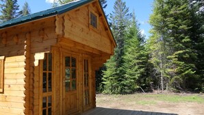 Una baita di legno con una veranda, ampie finestre e uno sfondo boschivo.