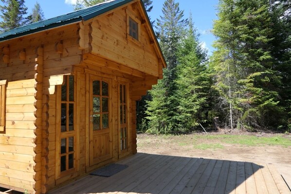 A wooden cabin with a deck, large windows, and a forest backdrop.
