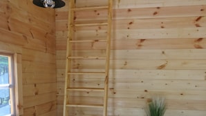 Interno di una baita in legno con un divano, una scala, un tavolino con cassetti e una finestra.