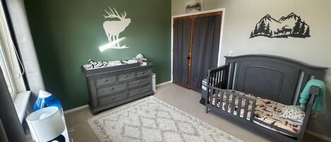 Quarto com berço, cómoda, ventoinha no teto e um adesivo de parede com um alce.