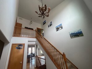 Una escalera con barandillas de madera que conduce a un segundo piso, un candelabro y un comedor con vistas al exterior.