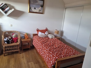 A bedroom with a wooden bed, a wicker chair with stuffed toys, a nightstand with a lamp, and a painting on the wall. - House 300 m from the ocean. Ocean view from the upper floor (Sarzeau)