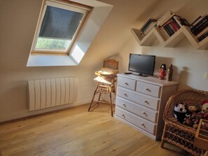 A room with a sloped ceiling, a window, a radiator, a television, a dresser, and a shelf with books. - House 300 m from the ocean. Ocean view from the upper floor (Sarzeau)