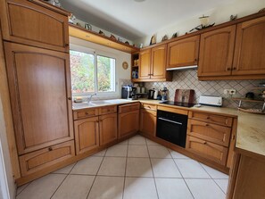 A kitchen with wooden cabinets, a dishwasher, a coffee maker, and a window with a view of trees. - House 300 m from the ocean. Ocean view from the upper floor (Sarzeau)