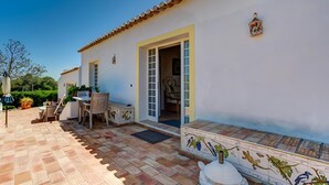 A white building with a tiled patio, a dining area with chairs and a table, and a door leading to an interior space. - Peaceful Algarve Couple Escape With Pool (Portimão)