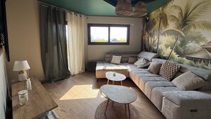 A living room with a sofa, a coffee table, a lamp, and a window with curtains. - Villa 5 bedrooms, Bali style with pool and jacuzzi, land 1700 m², near lake (Ambronay)