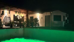 A nighttime view of a house with a pool, outdoor seating, and hanging lights. - Villa 5 bedrooms, Bali style with pool and jacuzzi, land 1700 m², near lake (Ambronay)