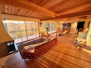 A spacious living area with a large window, a sofa, a dining table, and a kitchen area. - Spacious Hillside Mid-century Designer Home with Views (Glendale)