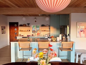 A modern kitchen with a central island, wooden ceiling, and a dining area with chairs and a table. - Spacious Hillside Mid-century Designer Home with Views (Glendale)