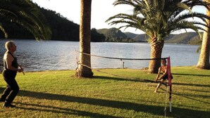 Un espace délimité par un filet, avec un filet de volley-ball, des palmiers et un lac en arrière-plan.