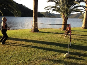 A netted area with a volleyball net, palm trees, and a lake in the background. - Water Front Cabin on the Hawkesbury (Sydney)