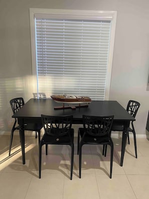 A dining area with a rectangular table, four chairs, and a window with blinds. - Water Front Cabin on the Hawkesbury (Sydney)