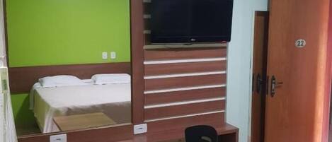 A room with a bed, a desk with a chair, a television mounted on the wall, and a door with a number.