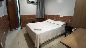 A single-bed room with a wooden door, an air conditioning unit, a table, and a chair. - Hotel do Porto (Porto Velho)