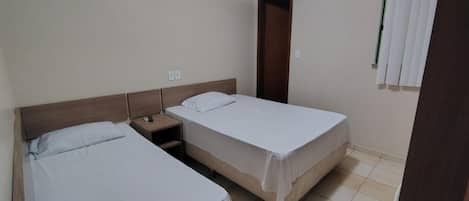 A room with two single beds, a wooden headboard, a nightstand, and a window with blinds.