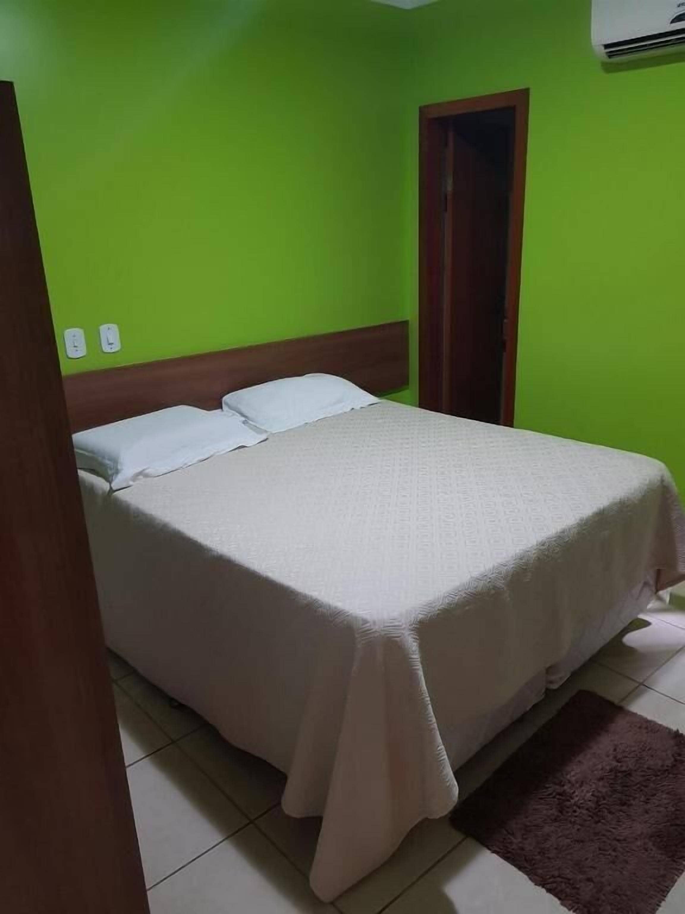 Una cama individual con cubrecama blanco en una habitación con paredes verdes y una puerta marrón.