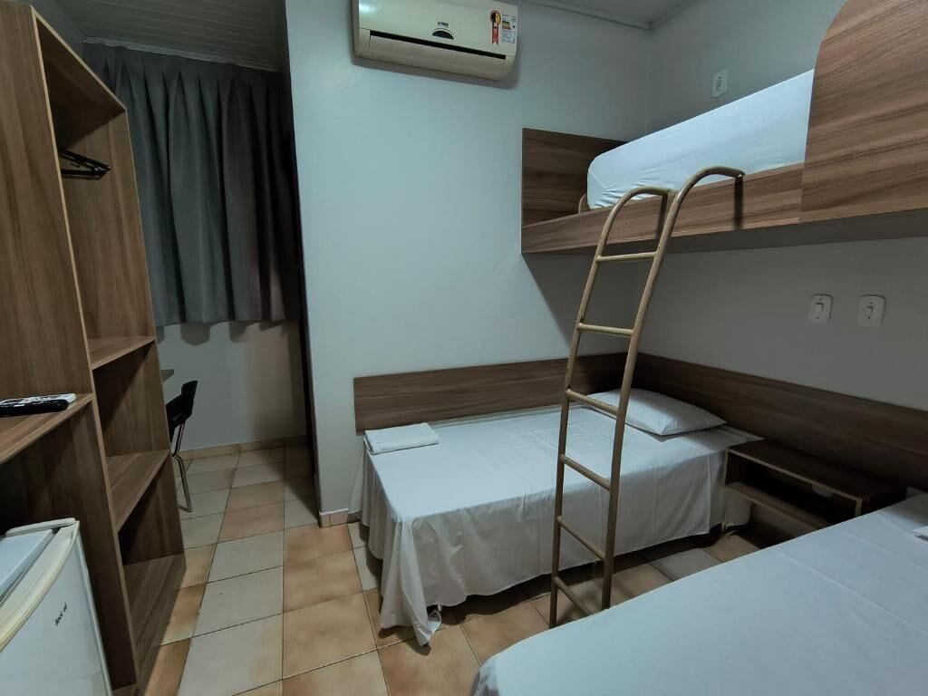 A room with bunk beds, a ladder, a small table, a shelf, and an air conditioning unit.