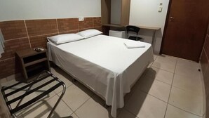 A hotel room with a bed, a small table, a chair, a wardrobe, and a door. - Hotel do Porto (Porto Velho)