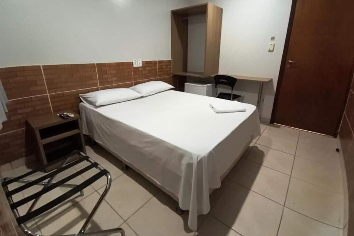 Una habitación de hotel con cama, una mesita, una silla, un armario y una puerta.