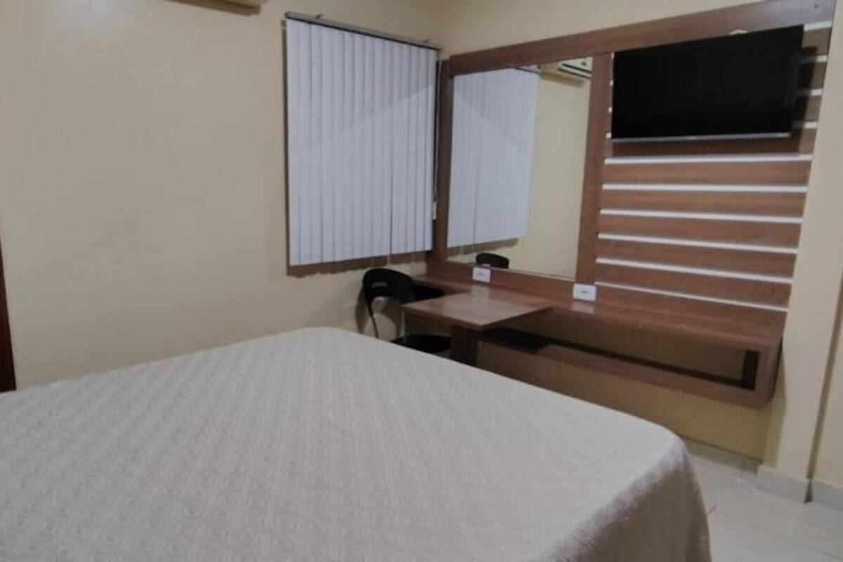 Un dormitorio con cama, escritorio, silla, ventana con persianas y puerta.