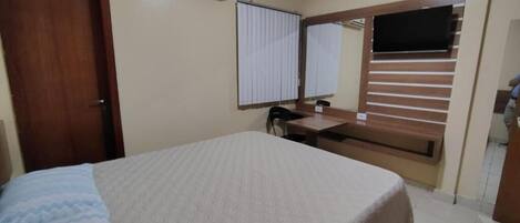 Une chambre à coucher comprenant un lit, un bureau, une chaise, une fenêtre avec des stores et une porte.