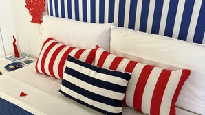 Un lit avec une literie à rayures et des oreillers, une décoration en corail rouge et un objet en forme de cœur posé sur le lit.