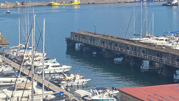 Un port de plaisance avec des bateaux amarrés, une jetée et une montagne qui se profile à l’horizon.