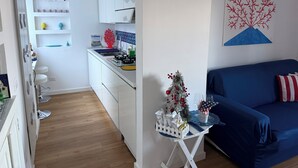 Une cuisine moderne avec des meubles blancs, un coin repas doté d’un canapé bleu et une petite table blanche sur laquelle est placé un sapin de Noël.