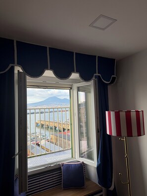 Una stanza con una finestra che si affaccia su un porto, un termosifone e una lampada a righe.