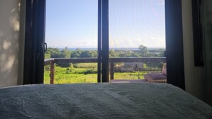 Een slaapkamer met een groot raam, een bed en uitzicht op een groen landschap.