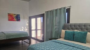 Een slaapkamer met een bed, een extra bed, een raam met gordijnen en een schilderij aan de muur.