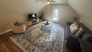 Ein Wohnzimmer mit Fernseher, Deckenventilator, Sofa, Couchtisch und einem gemusterten Teppich.