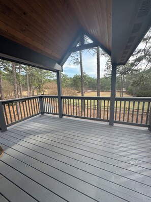 Un espace extérieur abrité, doté d’un plafond en bois, d’une rambarde en métal et offrant une vue sur un paysage boisé.