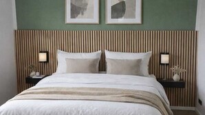 Um quarto com uma cama, duas mesas de cabeceira, uma cabeceira e duas pinturas abstratas emolduradas na parede.