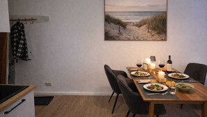 Uma sala de jantar com mesa posta para dois, apresentando uma pintura de praia, uma vela e uma garrafa de vinho.