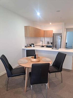 A modern kitchen with a central island, black chairs, and a round table. - Opposite Stadium 2BR CBD with Parking - Stadium Central 206 (Christchurch)