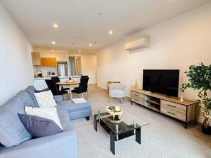 A modern living room with a sofa, coffee table, TV, and a dining area in the background. - Opposite Stadium 2BR CBD with Parking - Stadium Central 206 (Christchurch)
