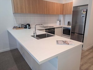 A modern kitchen with white countertops, wooden cabinets, stainless steel appliances, and a built-in oven. - Opposite Stadium 2BR CBD with Parking - Stadium Central 206 (Christchurch)
