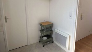 A corner room with a white door, a white cabinet above, a small metal cart with shelves, and a white vent. - 5 minutes from the train station! Bright and spacious apartment (Romilly-sur-Seine)