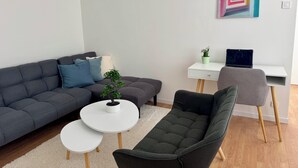 A modern living room with a grey sofa, a small round table, a grey armchair, and a white desk with a laptop. - 5 minutes from the train station! Bright and spacious apartment (Romilly-sur-Seine)