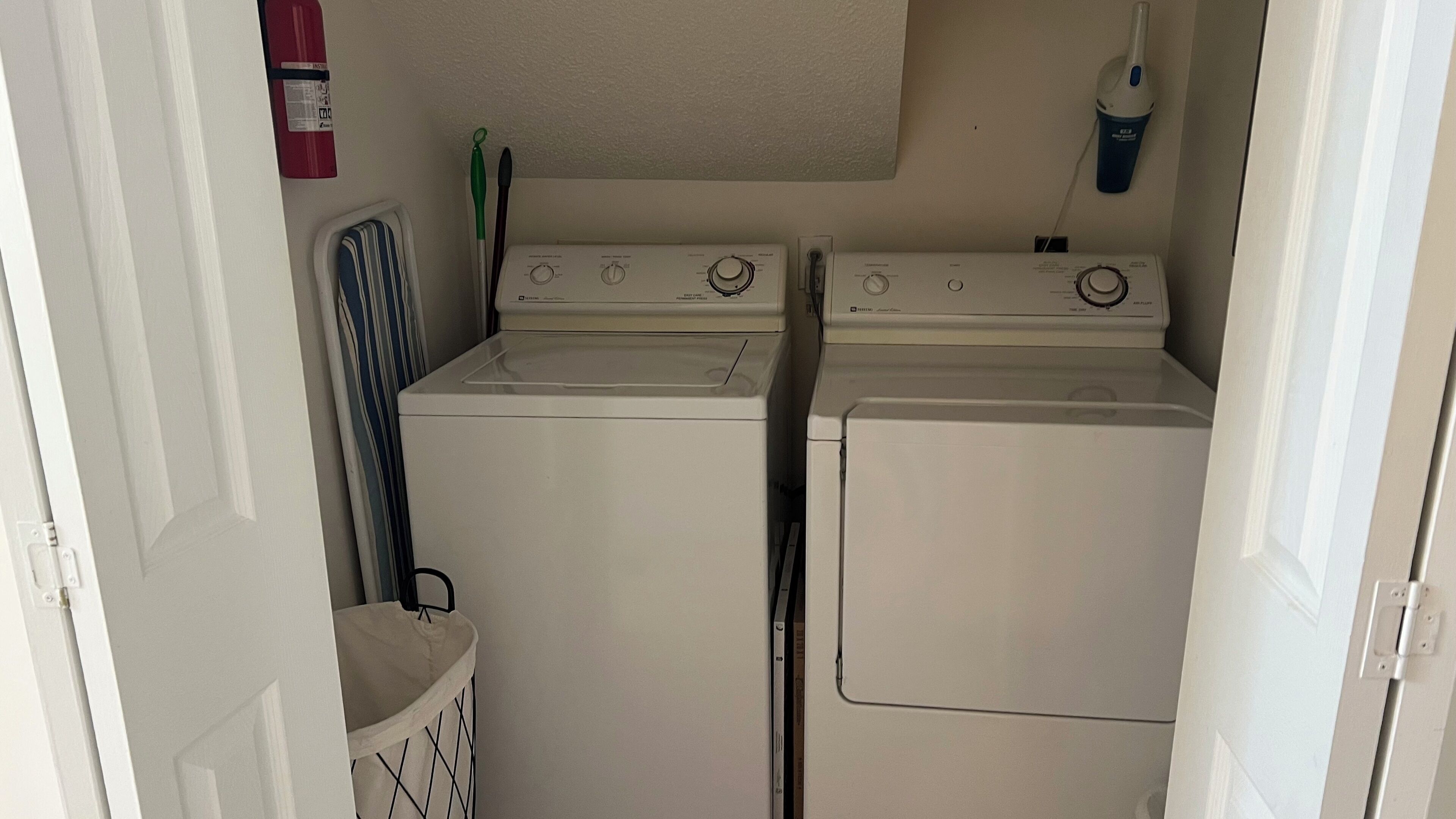 A laundry room with two stacked washers and dryers, a fire extinguisher, and a hanging rack.